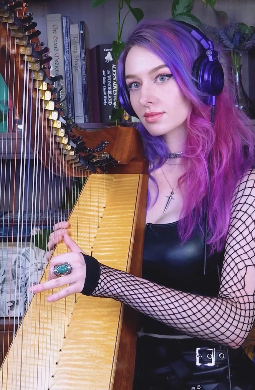 Young woman with pink and purple hair playing a harp and smiling.